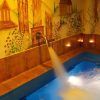 El agua fluye hacia una serena piscina azul, rodeada de un mural de edificios antiguos y naturaleza, creando una escapada tranquila que recuerda a la "Oferta Lunes a Viernes de sesión de Spa en Aqua Urban Spa Barcelona. - ForTwo - Planes para parejas