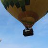 Captura un primer plano de un vibrante globo aerostático amarillo y verde en vuelo, con uno más pequeño detrás, contra el cielo azul claro. Disfruta de esta fascinante escena durante un vuelo en globo con Eolofly en Aranjuez sobre pintorescos paisajes. - ForTwo - Planes para parejas