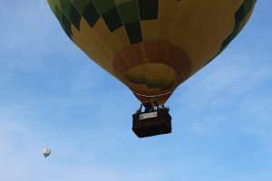 Captura un primer plano de un vibrante globo aerostático amarillo y verde en vuelo, con uno más pequeño detrás, contra el cielo azul claro. Disfruta de esta fascinante escena durante un vuelo en globo con Eolofly en Aranjuez sobre pintorescos paisajes. - ForTwo - Planes para parejas