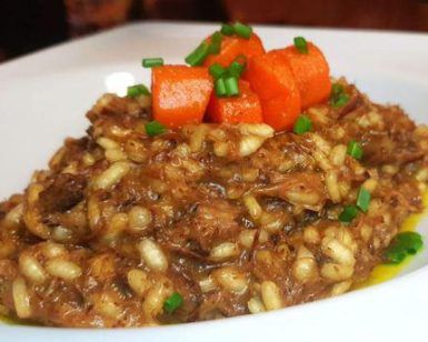 En el Restaurante Galipán (Valencia), disfrute de un lujoso risotto con tiernos trozos de carne, vibrantes zanahorias cortadas en cubitos y frescas hierbas verdes, servido artísticamente en un tazón blanco. - ForTwo - Planes para parejas