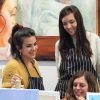 Tres mujeres con delantales de rayas disfrutan de un animado "Arte y Vino: Taller de Pintura y Vino" en Barcelona, sonriendo e interactuando entre sí. - ForTwo - Planes para parejas