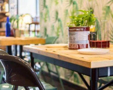 Esta moderna cafetería, con mesas de madera, sillas verdes y un centro de mesa con plantas, rezuma el ambiente del Restaurante Artefacto (Sevilla). Un papel pintado con estampado de hojas adorna las paredes, realzando el encantador ambiente de los cafés sevillanos. - ForTwo - Planes para parejas