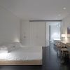 La habitación minimalista del Hotel Atrio (Cáceres) incluye cama, escritorio y silla. Tiene suelo oscuro y paredes blancas, con una serena vista al baño, combinando sencillez y elegancia. - ForTwo - Planes para parejas