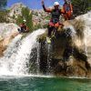 Una persona con casco salta desde una pequeña cascada a las cristalinas aguas de la Alpujarra, mientras otros dos observan, cautivados por esta emocionante experiencia de "Barranquismo en Granada-Poqueira, en la Alpujarra". - ForTwo - Planes para parejas