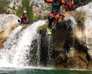 Una persona con casco salta desde una pequeña cascada a las cristalinas aguas de la Alpujarra, mientras otros dos observan, cautivados por esta emocionante experiencia de "Barranquismo en Granada-Poqueira, en la Alpujarra". - ForTwo - Planes para parejas
