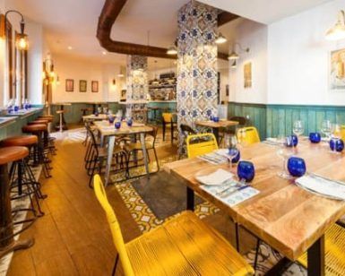 El restaurante Bache San Pedro (Sevilla) cuenta con acogedoras mesas de madera, cristalería azul vibrante, sillas amarillas y azulejos de pared decorativos que encarnan el encanto de Sevilla. - ForTwo - Planes para parejas