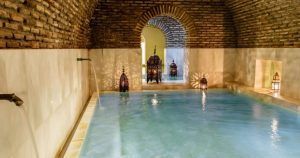 La piscina cubierta cuenta con un techo arqueado de ladrillo que crea un ambiente medina mudéjar, mientras que las linternas ornamentadas brindan un brillo cálido similar al Baño árabe con masaje relajante en Medina Mudéjar, Toledo. - ForTwo - Planes para parejas