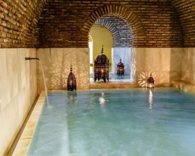 La piscina cubierta cuenta con un techo arqueado de ladrillo que crea un ambiente medina mudéjar, mientras que las linternas ornamentadas brindan un brillo cálido similar al Baño árabe con masaje relajante en Medina Mudéjar, Toledo. - ForTwo - Planes para parejas