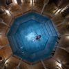 Una persona flota en una piscina octogonal en Baño en Pareja Hammam Al Ándalus Málaga Baños Árabes, rodeada de columnas e iluminación tenue, creando el ambiente sereno de los antiguos Baños Árabes. - ForTwo - Planes para parejas