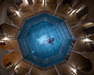 Una persona flota en una piscina octogonal en Baño en Pareja Hammam Al Ándalus Málaga Baños Árabes, rodeada de columnas e iluminación tenue, creando el ambiente sereno de los antiguos Baños Árabes. - ForTwo - Planes para parejas