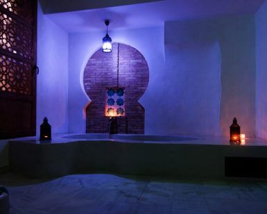 El ambiente, con linternas, nichos arqueados, patrones intrincados y una suave iluminación azul en un baño de estilo marroquí, da vida a la tranquilidad de un "Hammam privado en pareja en los baños árabes de Al-Haram (Granada)". - ForTwo - Planes para parejas