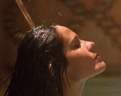Bajo la suave luz de un espacio poco iluminado, una persona con el cabello mojado disfruta del agua relajante de la ducha, que recuerda a un baño turco en Córdoba: baño árabe con masaje MIMMA. - ForTwo - Planes para parejas