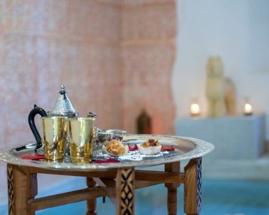 Una bandeja con tetera, tazas y pasteles junto a la piscina, bañada por la luz de las velas, evoca la serena elegancia del “Hammam nocturno en los baños árabes de Al-Haram (Granada)” en una estancia bellamente decorada. - ForTwo - Planes para parejas