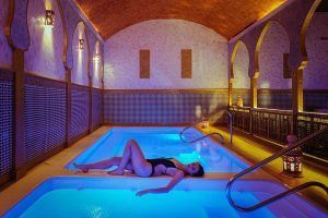 Relajarse junto a una piscina cubierta iluminada con techo abovedado y azulejos decorativos se siente como entrar en el Baño árabe para dos con masaje completo en Medina Aljarafe (Sevilla), que ofrece una escapada serena. - ForTwo - Planes para parejas