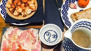 Una mesa con platos variados como pasta, pan y salsa de la Pulpería Can Lampazas Para-lel (Barcelona) con platos adornados con patrones azules. - ForTwo - Planes para parejas