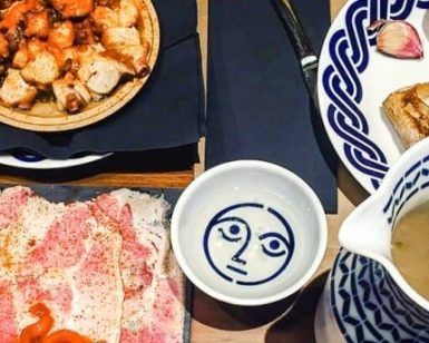 Una mesa con platos variados como pasta, pan y salsa de la Pulpería Can Lampazas Para-lel (Barcelona) con platos adornados con patrones azules. - ForTwo - Planes para parejas