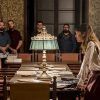 En una sala vintage, la gente se reúne alrededor de una gran mesa cubierta de papeles, cautivada por dos mujeres que desentrañan la Cena Enigma, que recuerda a la "Cena a lo Sherlock Holmes con la Cena Enigma de Sternalia" en Barcelona. - ForTwo - Planes para parejas