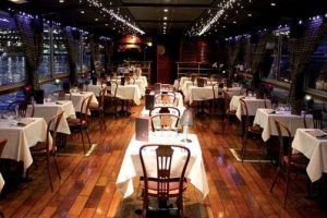 Experimente un elegante ambiente de restaurante con pisos de madera, manteles blancos y luces de cadena mientras disfruta de impresionantes vistas al mar de los barcos deslizándose con el "Paseo por el Sena en barco con cena de lujo (París)" para una velada perfecta. - ForTwo - Planes para parejas