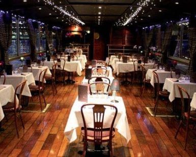 Experimente un elegante ambiente de restaurante con pisos de madera, manteles blancos y luces de cadena mientras disfruta de impresionantes vistas al mar de los barcos deslizándose con el "Paseo por el Sena en barco con cena de lujo (París)" para una velada perfecta. - ForTwo - Planes para parejas