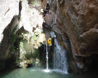 En una emocionante aventura, alguien desciende en rápel por una cascada entre cañones rocosos, exuberante vegetación y aguas cristalinas similar al Pack multiaventura en pareja en Madrid. - ForTwo - Planes para parejas