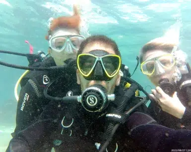 Tres buceadores con trajes de neopreno y gafas posan para un selfie grupal durante su "Bautizo de buceo con Freeandivers (Barcelona). - ForTwo - Planes para parejas