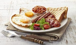 Disfrute de un brunch romántico en el Restaurante Gaztedi-Berria, que ofrece un desayuno inglés completo con huevos, tocino, salchichas, frijoles, tostadas y ensalada servido en un plato blanco con cubiertos. - ForTwo - Planes para parejas