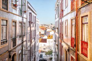 Explorar una calle estrecha en Mouraria, bordeada de edificios coloridos, revela un paisaje urbano pintoresco bajo un cielo azul claro como parte de la experiencia Visita a Mouraria y cena con concierto de fado (Lisboa). - ForTwo - Planes para parejas