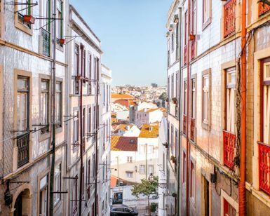 Explorar una calle estrecha en Mouraria, bordeada de edificios coloridos, revela un paisaje urbano pintoresco bajo un cielo azul claro como parte de la experiencia Visita a Mouraria y cena con concierto de fado (Lisboa). - ForTwo - Planes para parejas