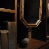 Estantes de madera tenuemente iluminados con libros antiguos, una botella inclinada y un espejo con marco de madera que refleja la oscuridad evocan el ambiente misterioso de Capitan Pessoa - Un juego para 2 de Retobox Escape Room (Barcelona). - ForTwo - Planes para parejas