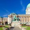 Explora la belleza arquitectónica del Castillo de Buda en Budapest, con cúpulas verdes, una fachada ornamentada y una estatua de jardín bajo un cielo azul claro con el "Tour por el castillo de Buda (Budapest). - ForTwo - Planes para parejas