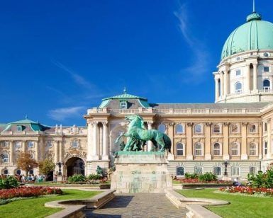 Explora la belleza arquitectónica del Castillo de Buda en Budapest, con cúpulas verdes, una fachada ornamentada y una estatua de jardín bajo un cielo azul claro con el "Tour por el castillo de Buda (Budapest). - ForTwo - Planes para parejas