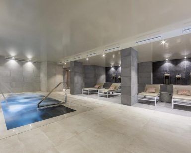 El moderno interior del spa del Hotel Cataluña ofrece una pequeña piscina, tumbonas e iluminación tenue. Los huéspedes podrán relajarse con la experiencia "Circuito de aguas, cava y masaje de esencias para parejas" en Granada. - ForTwo - Planes para parejas