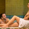 En una tranquila sala de azulejos del Circuito de spa con masaje en pareja en Granada, un hombre en la piscina sonríe cálidamente a una mujer sentada en una toalla. Su relajación se integra a la perfección con el ambiente acogedor, ideal para desconectar juntos. - ForTwo - Planes para parejas