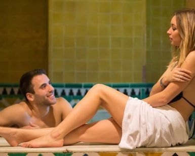En una tranquila sala de azulejos del Circuito de spa con masaje en pareja en Granada, un hombre en la piscina sonríe cálidamente a una mujer sentada en una toalla. Su relajación se integra a la perfección con el ambiente acogedor, ideal para desconectar juntos. - ForTwo - Planes para parejas