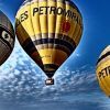 Tres globos aerostáticos con la marca Globus Kon Tiki flotan con gracia bajo un cielo azul salpicado de nubes, ofreciendo una inolvidable "Oferta de vuelo en globo en Cataluña con Globus Kon Tiki" sobre los paisajes escénicos de Cataluña. - ForTwo - Planes para parejas