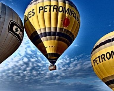 Tres globos aerostáticos con la marca Globus Kon Tiki flotan con gracia bajo un cielo azul salpicado de nubes, ofreciendo una inolvidable "Oferta de vuelo en globo en Cataluña con Globus Kon Tiki" sobre los paisajes escénicos de Cataluña. - ForTwo - Planes para parejas
