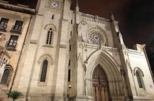 Explora la fachada de la catedral de estilo gótico con su gran rosetón y sus ornamentadas puertas de madera, iluminada por la noche, en el "Tour gratuito de los misterios y leyendas (Bilbao)" para descubrir las historias grabadas en sus piedras. - ForTwo - Planes para parejas