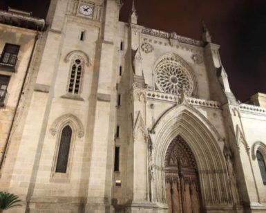 Explora la fachada de la catedral de estilo gótico con su gran rosetón y sus ornamentadas puertas de madera, iluminada por la noche, en el "Tour gratuito de los misterios y leyendas (Bilbao)" para descubrir las historias grabadas en sus piedras. - ForTwo - Planes para parejas