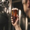 En el corazón de Barcelona, una persona inspecciona un vaso de cerveza ámbar durante "Visita y cata en La Cervecería de Poblenou", donde cada cerveza cuenta su propia historia. - ForTwo - Planes para parejas