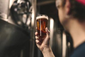 En el corazón de Barcelona, una persona inspecciona un vaso de cerveza ámbar durante "Visita y cata en La Cervecería de Poblenou", donde cada cerveza cuenta su propia historia. - ForTwo - Planes para parejas