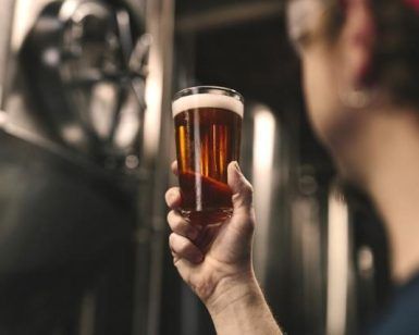 En el corazón de Barcelona, una persona inspecciona un vaso de cerveza ámbar durante "Visita y cata en La Cervecería de Poblenou", donde cada cerveza cuenta su propia historia. - ForTwo - Planes para parejas