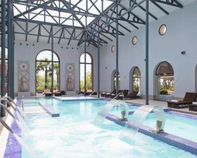 La piscina cubierta del Circuito Yhi Spa Meliá Villaitana (Alicante) cuenta con tumbonas, ventanas arqueadas con vigas de acero y elementos de agua en cascada, creando un ambiente sereno en este lujoso oasis. - ForTwo - Planes para parejas