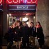 Un grupo de personas sonriendo y posando delante de un cartel iluminado de neón por la noche, listas para una velada de humor inolvidable en la bulliciosa entrada de Cómico Cómico en Barcelona para una Cena con espectáculo de humor. - ForTwo - Planes para parejas