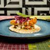 Taco de pescado frito con col morada y salsa en un plato azul en el Restaurante El Indiano Madrid-México, colocado sobre una mesa de mosaico colorido contra una pared geométrica. - ForTwo - Planes para parejas