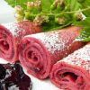 Crepes rosas espolvoreadas con azúcar glas, cubiertas con bayas y hojas en un plato blanco, reflejan la vitalidad del Taller de crepes de colores de Barcelona. - ForTwo - Planes para parejas