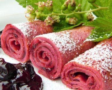 Crepes rosas espolvoreadas con azúcar glas, cubiertas con bayas y hojas en un plato blanco, reflejan la vitalidad del Taller de crepes de colores de Barcelona. - ForTwo - Planes para parejas