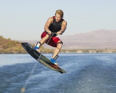 Una persona con un traje rojo practica wakeboard, elevándose sobre el agua en un día soleado, capturando la esencia de "Vive una auténtica experiencia de Wakeboard en Barcelona". - ForTwo - Planes para parejas