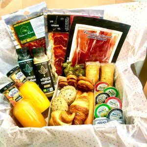 La canasta de regalo "Desayuno romántico a domicilio por Las Flores No se Comen" incluye paquetes de jamón, jugo, botellas de café, queso, pasteles y pães de queijo sobre un paño de lunares; ideal para un desayuno romántico a domicilio. - ForTwo - Planes para parejas