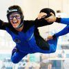 Una persona experimenta la emoción del paracaidismo indoor en Windoor, en Barcelona, vistiendo un traje azul y negro y sonriendo mientras un instructor le ayuda en el túnel de viento. - ForTwo - Planes para parejas