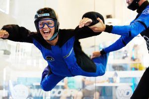 Una persona experimenta la emoción del paracaidismo indoor en Windoor, en Barcelona, vistiendo un traje azul y negro y sonriendo mientras un instructor le ayuda en el túnel de viento. - ForTwo - Planes para parejas